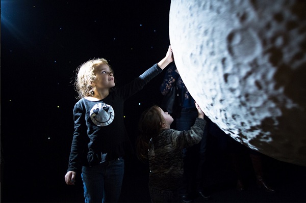 Girl reaching out to touch a moon installation at an exhibit.